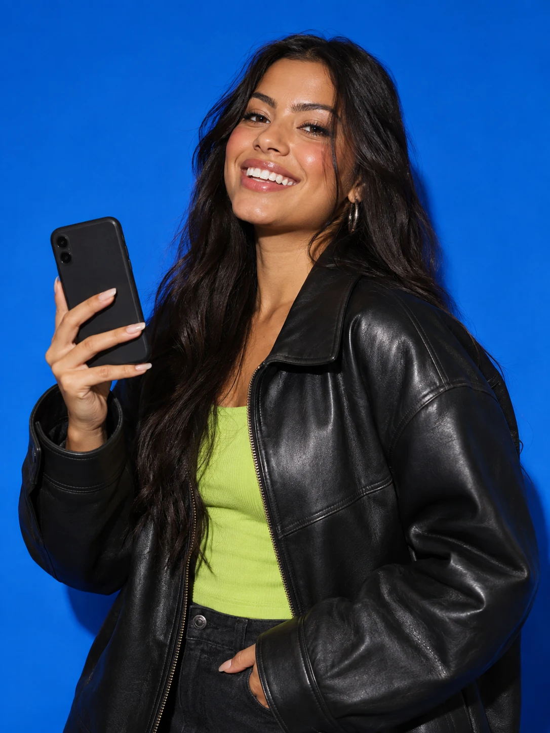 Modelo adulta em campanha editorial, com jaqueta preta e celular, diante de fundo azul